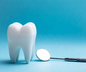 Close-up Of Tooth With Dental Mirror Over Blue Background